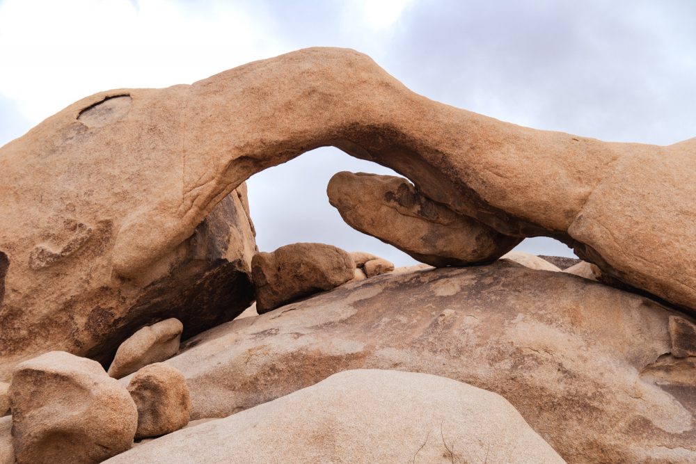 A rock formation with an arch set among a bluish sky, in Joshua Tree National Park