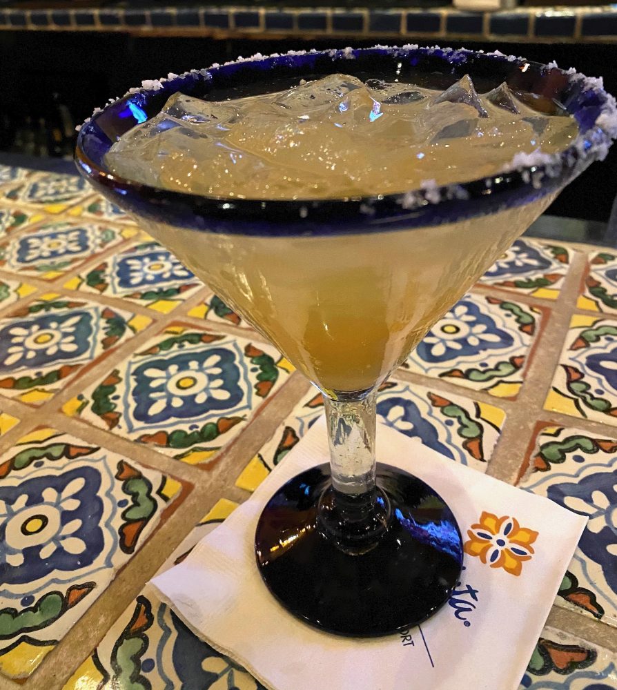 A large margarita alcoholic drink on top of a cocktail napkin on a southwest style tiled counter.