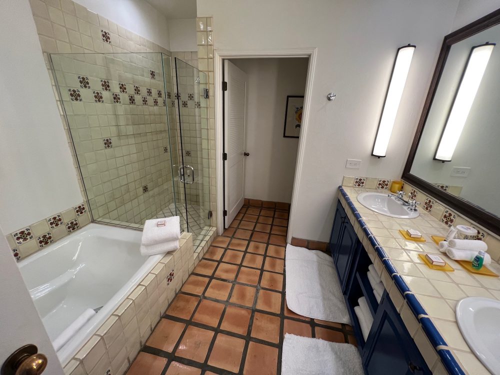 A southwestern styled bathroom. On the left is a large tub and separate shower stall. On the right is a tiled counter with two sinks and a large mirror.