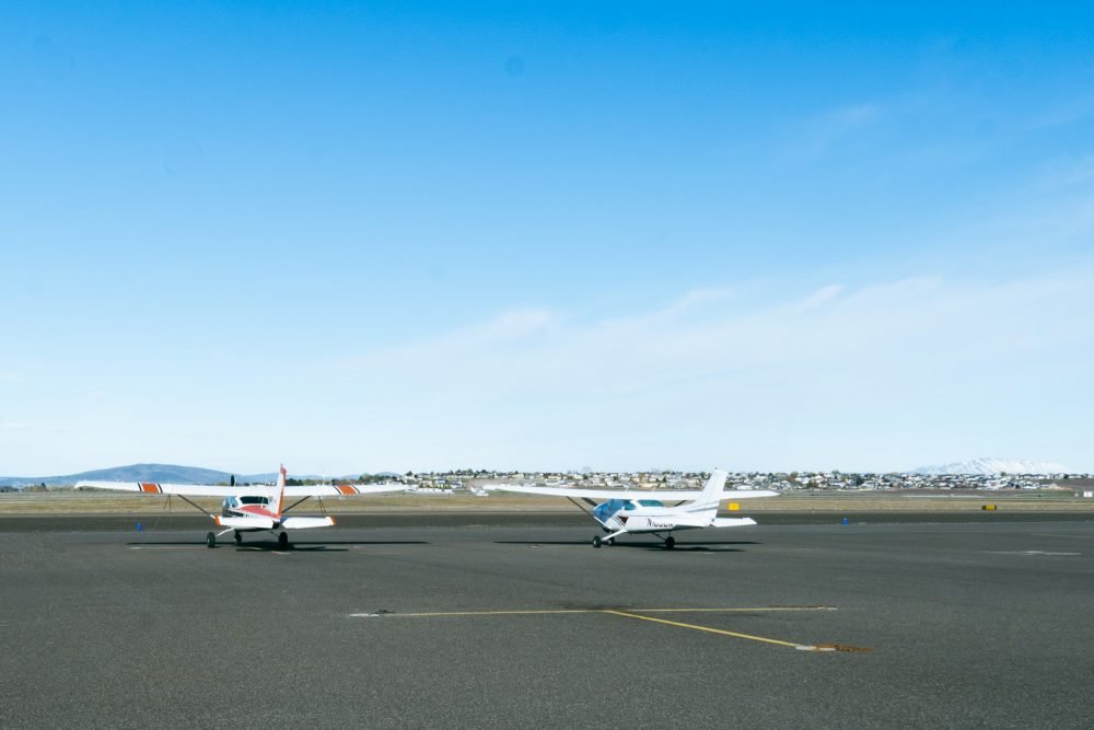 Two small single-engine propeller planes side by side on the tarmac at an airport.