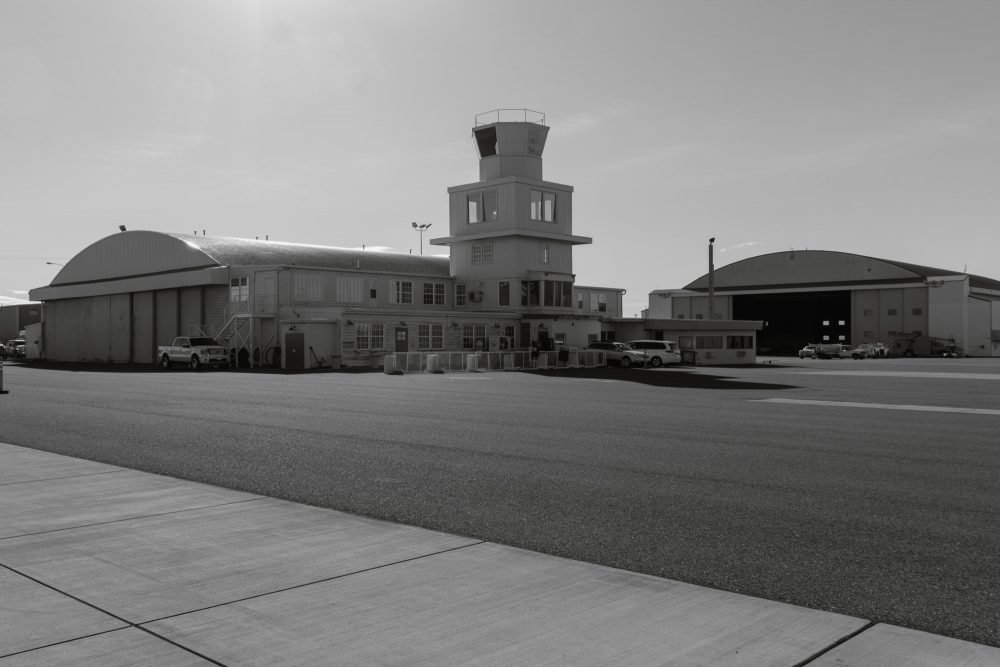 Two airport hangars and a four story air traffic control tower in black and white.